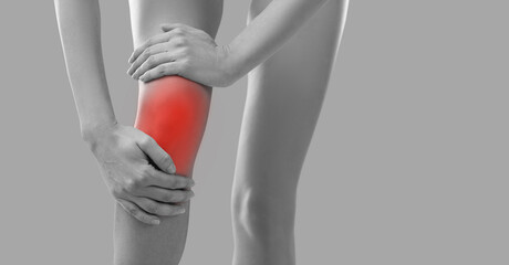 Woman whose knee is hurting holding her hand on injured kneecap area. Cropped BW shot of human legs...
