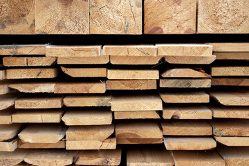 Roughly processed boards lie in a stack. Close-up view of the ends of the boards. Softwood lumber in a stack in the sun.