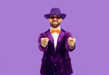 Portrait of excited male entertainer in velvet suit isolated on purple studio background point at...