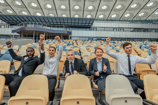 Excited people in business suits sitting in fan zone of stadium