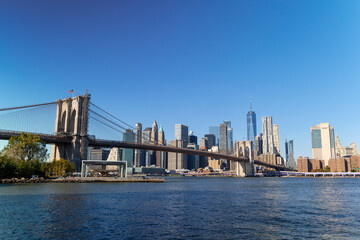Fototapeta premium Lower Manhattan skyscraper stands behind Brooklyn Bridge beyond the East River on November 5, 2021 in New York City NY USA. NYC Ferry runs on East River.