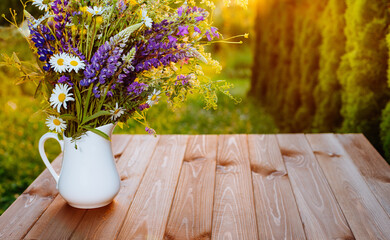 Beautiful meadow summer flowers in a vase on a sunny wooden patio. chamomiles bouquet in sunset sunlight. Copy space. Romantic picnic or weekend
