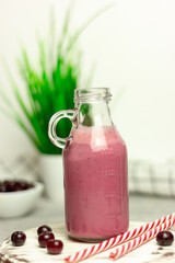 A bottle of cherry smoothies on a white background, cherries in bulk and in a plate. Morning summer breakfast