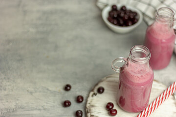 A bottle of cherry smoothies on a white background, cherries in bulk and in a plate. Morning summer breakfast
