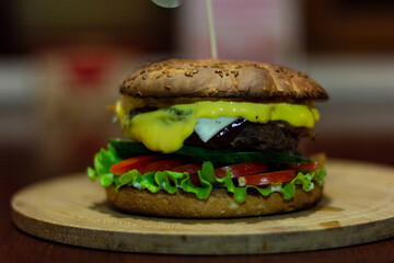 Burger from a meat patty with fresh cucumbers, tomatoes and cheese. White bun sprinkled with sesame seeds. Close-up