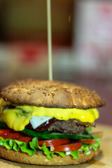 Burger from a meat patty with fresh cucumbers, tomatoes and cheese. White bun sprinkled with sesame seeds. Close-up