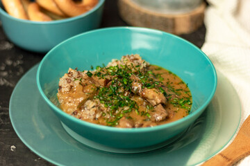 Buckwheat with meat and sauce in a blue plate, sprinkled with herbs. On a dark table. The concept of lunch, or a hearty dinner
