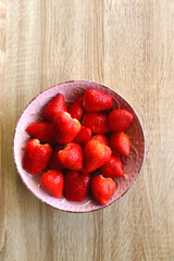 Pink bowl full of fresh strawberries on wooden table. Flat lay.