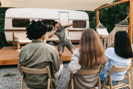 Multiracial Young Friends Playing Charades Near Motorhome During Outdoor Party