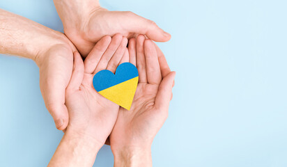 female and male hands hold a heart painted in the colors of the Ukrainian flag on a blue background