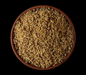Dry bulgur pile in clay pot isolated on black, top view