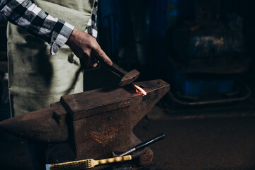 The blacksmith manually forging the red-hot metal on the anvil in smithy.