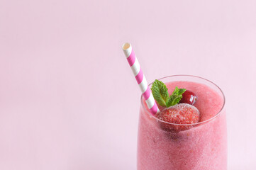 Pink homemade smoothie or yogurt with frozen strawberries and cranberries with a mint leaf and straw. Close-up, part of a glass. Selective focus with natural light and copy space on pink background