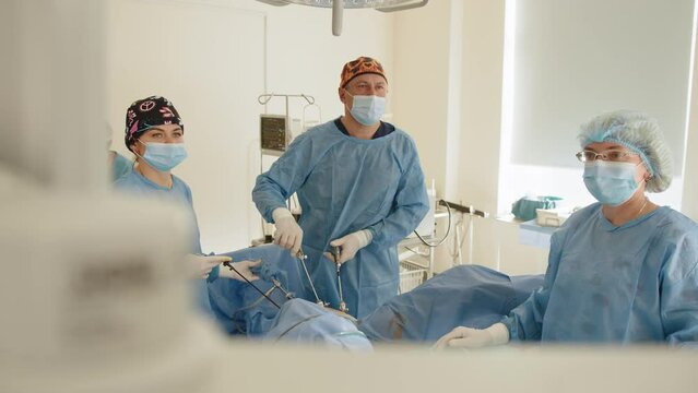 Surgeons team preforming operation uterus removal in hospital operating theater, male surgeon operating patient working with surgical laparoscopy instruments. Gynecology