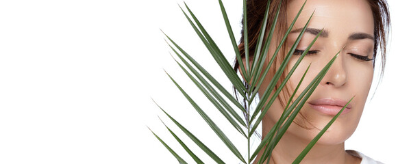 Fototapeta premium Beauty and Skincare Concept. Beautiful natural young woman face with nude makeup on a flawless skin with a palm leaf