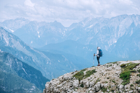 Woman trekker with backpack and trekking poles on the hill enjoying picturesque Dolomite Alps view near Tre Cime di Lavaredo formation in South Tyrol, Italy. Active people and mountain concept.
