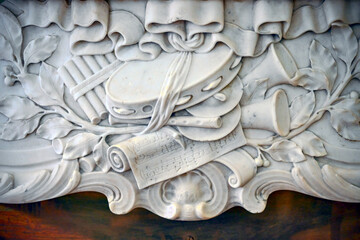A close-up of a fragment of a marble wall with carvings in the form of musical instruments. Decorative stone carving.
