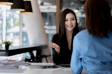 Obraz premium Atmosphere in the office of a startup company, two female employees are discussing, brainstorming ideas to working on summaries and marketing plans to increase sales and prepare reports to managers.