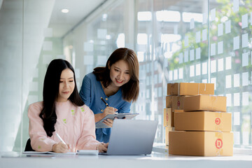 Two owners of an online store on the website are preparing parcels to send to customers following orders from the web page, they check the information and prepare for delivery to the customers.