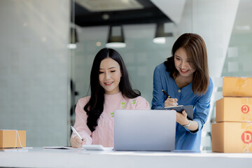 Two owners of an online store on the website are preparing parcels to send to customers following orders from the web page, they check the information and prepare for delivery to the customers.