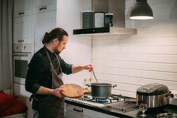 A male cook is cooking at the stove at home in the kitchen
