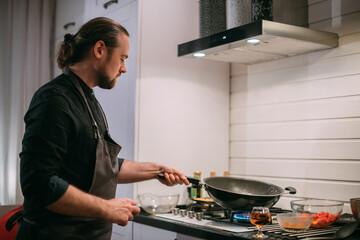 A male cook is cooking at the stove at home in the kitchen