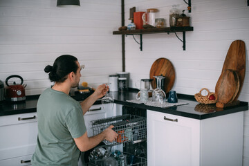Weekend homework. A young man takes out clean dishes from the dishwasher in the kitchen at home.