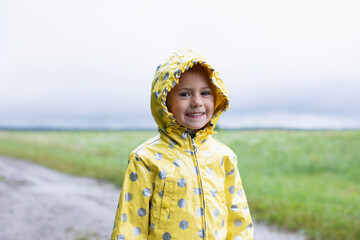 Portrait of a happy child in a yellow raincoat on the nature