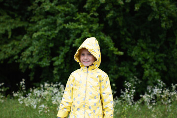 Funny little girl in a yellow raincoat in the spring forest on a walk