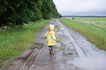 A small child in a yellow raincoat runs on a dirt road and mud