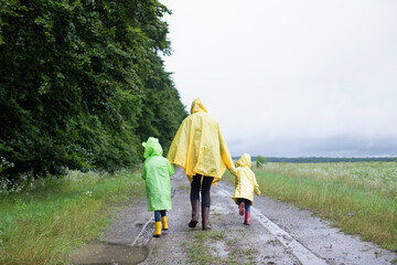 Mother and two children sisters in raincoats walk in the rain in nature. Family spring walk