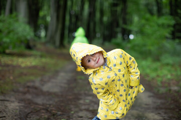Funny little girl in a yellow raincoat smiling in the spring forest