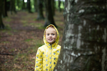 Portrait of a funny girl in a yellow raincoat in the woods
