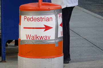 Sign duck taped to an orange traffic warning barrel with an arrow indicating a pedestrian walkway