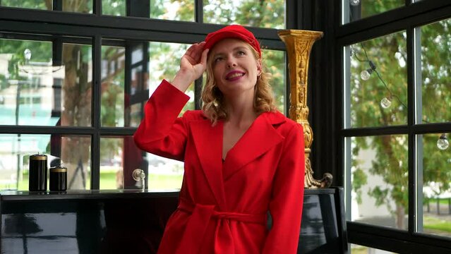 Attractive girl in red jacket and cap posing in cafe. Woman sends an air kiss. Concept: fashion and style. 