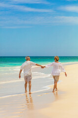 Mature couple holding hands walking along shoreline Bahamas