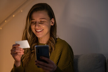 Fototapeta premium Woman holding credit card and using smartphone while online shopping at home