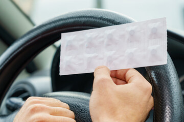 Pack of pills in the hands of the driver on a blurred background of the steering wheel in the car