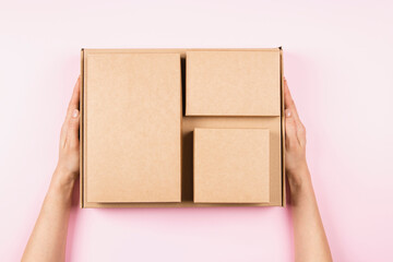 Top view to stack of cardboard boxes in female hands. Blank brown parcel boxes on pastel pink...