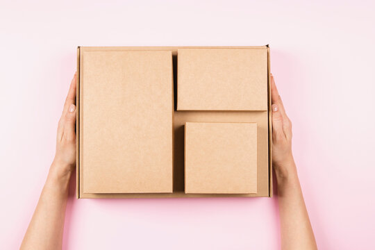 Top view to stack of cardboard boxes in female hands. Blank brown parcel boxes on pastel pink background. Packaging, shopping, free shipping, delivery concept