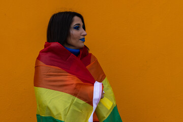 portrait of a young woman draped in a lgbt flag on a yellow background