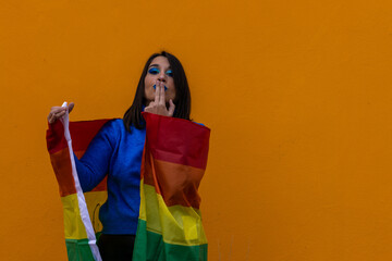 Young woman with LGBT flag blowing kiss on yellow background