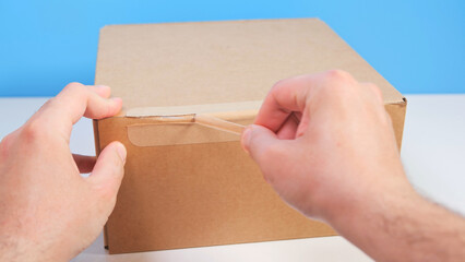 Close up man hand's opening cardboard box package by pulling tear tape. Unboxing brown cardboard...