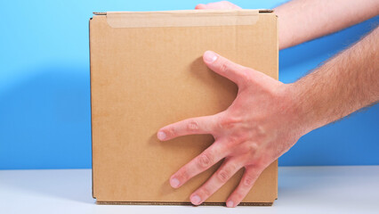 A parcel with humanitarian aid. A man puts a cardboard box with provisions on the white table.