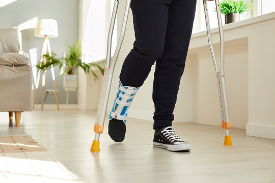 Unwell man with bandage on injured leg walk on crutches at home. Unhealthy sick injured male wear protective sling or splint on foot after accident or trauma. Injury and rehabilitation concept.