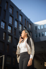 Young businesswoman using phone outdoors at the modern office district