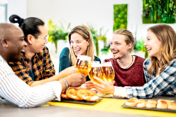 Happy smiling young friends enjoying and toasting beer pint on happy hour at pub - Friendship concept with multiracial people having fun together.