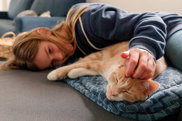 An Young Adolescent girl lying on a couch finds comfort by snuggling close to and petting her cat