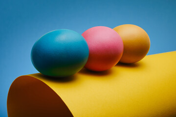 Colorful three Easter eggs on a rolled sheet of paper against a blue background