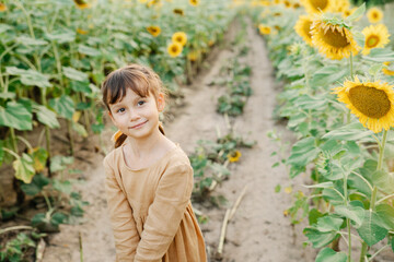 Portrait of little ukrainian girl wearing linen mustard dress standing in sunflower field.